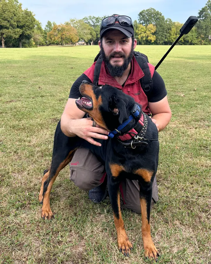Kelton Azuara-Walker kneeling in a park with a black-and-tan dog who looks up at him