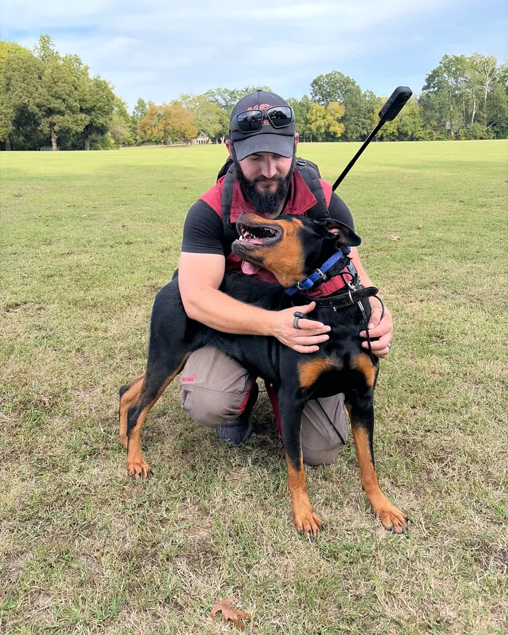 Kelton kneeling in a park, hugging a black-and-tan dog who looks up at him