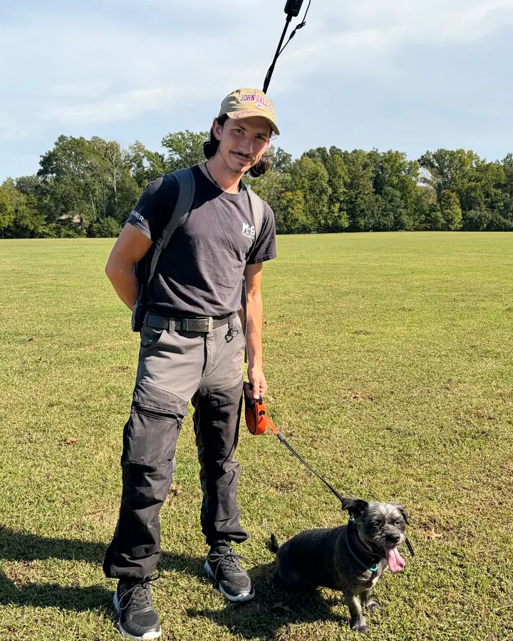Christian Scharphorn, Founder and Lead Behaviorist, standing in a park with a small dark dog on a leash