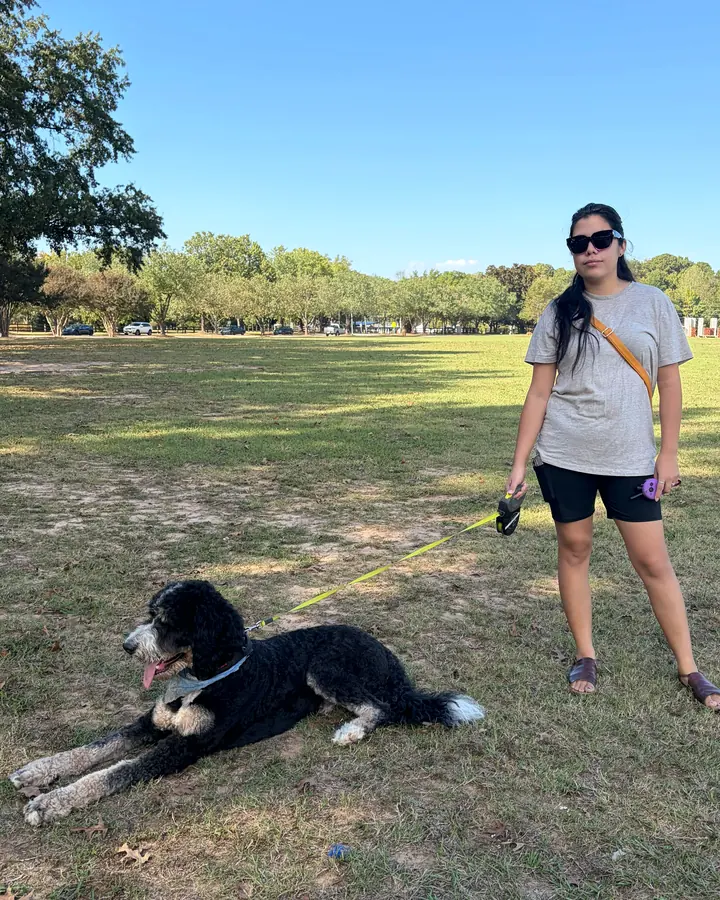 Claudia standing in a park while a black-and-white doodle lies in a down on a long line