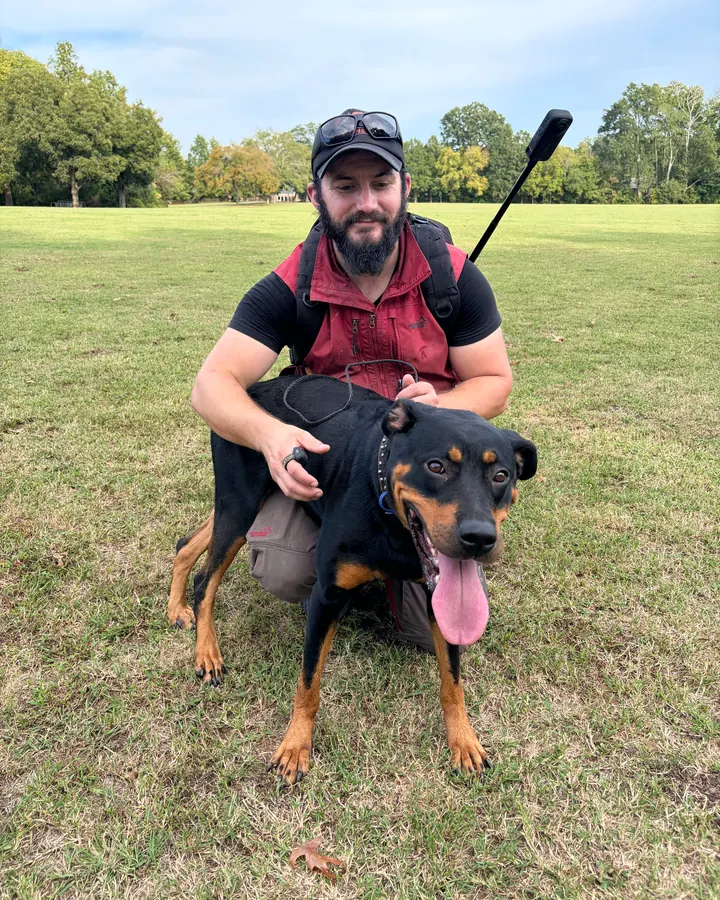 Kelton kneeling in a park with a black-and-tan dog